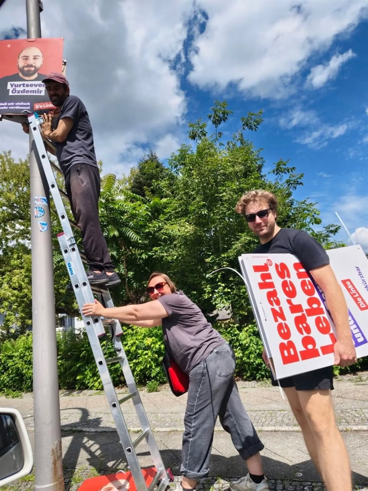 Plakate aufhängen im Kiez — eine Person auf der Leiter, daneben das Plakat „Bezahlbares Leben"