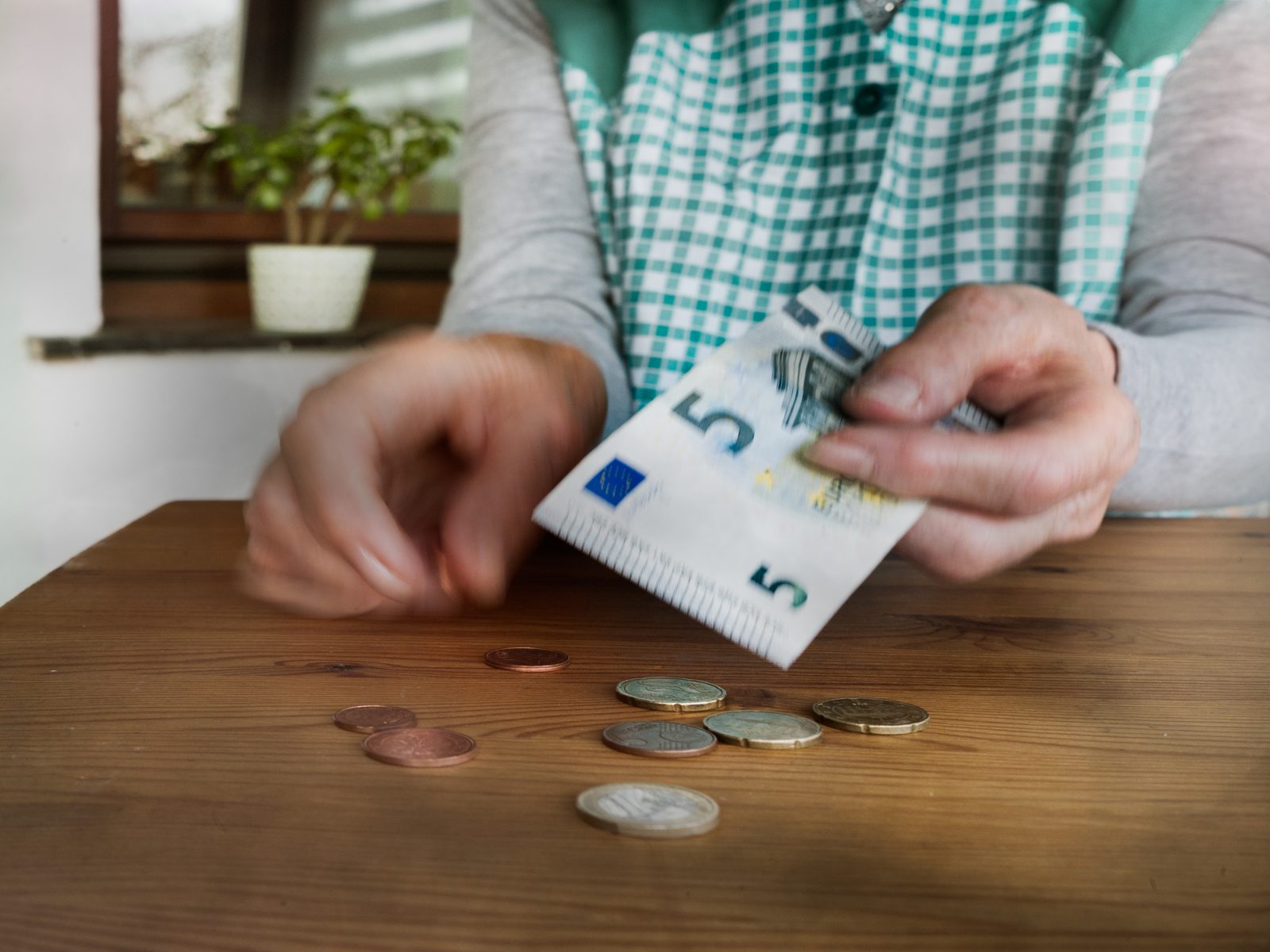 Hände zählen wenige Münzen und einen Fünf-Euro-Schein auf einem Tisch